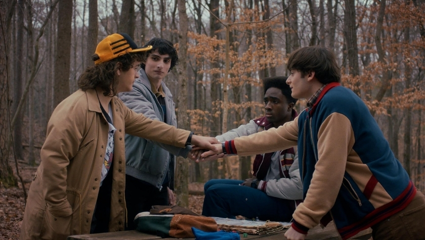 Cast of Stranger Things joining hands in the woods