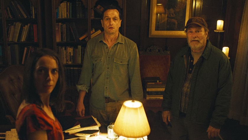 Tom and two other Widow's Bay residents gathered around a lamp-lit table in a dark, book-filled room