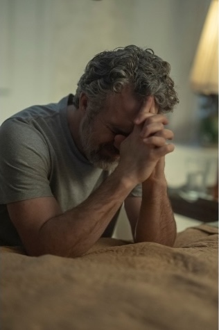 Tom Brandis (Mark Ruffalo) sits at the edge of a bed with his head bowed and hands clasped in a moment of despair in Task on HBO