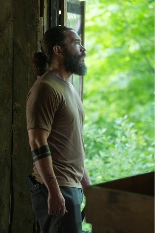 Robbie Pendergrass (Tom Pelphrey) stands alone in a doorway looking out at greenery in a contemplative moment from Task on HBO