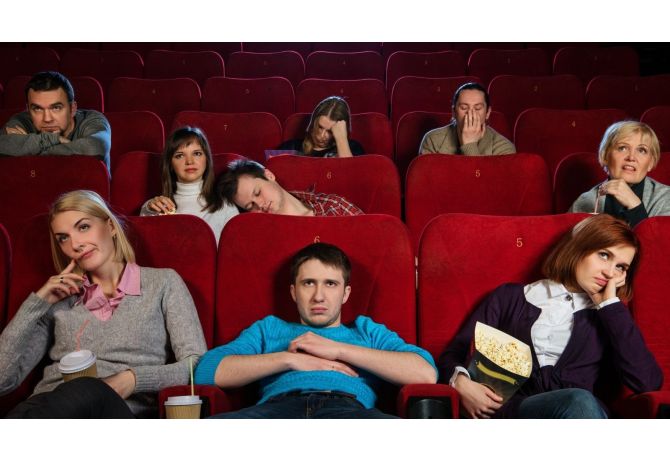 Group of people in a movie theater appearing bored or uninterested, with some yawning and others slouching in red seats.