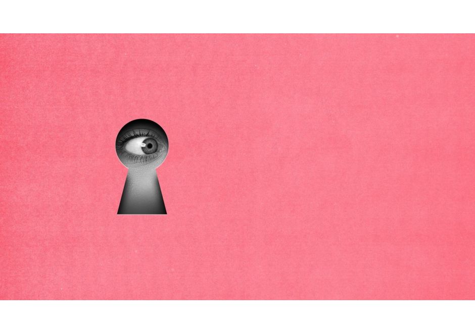 Close-up of a human eye looking through a keyhole on a pink background