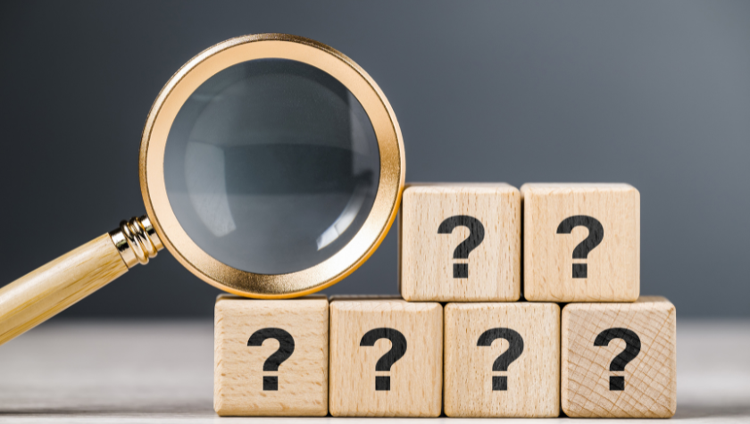 A golden magnifying glass resting on 6 blocks displaying question marks