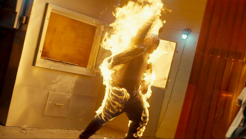 A person standing in a disheveled room enveloped in flames