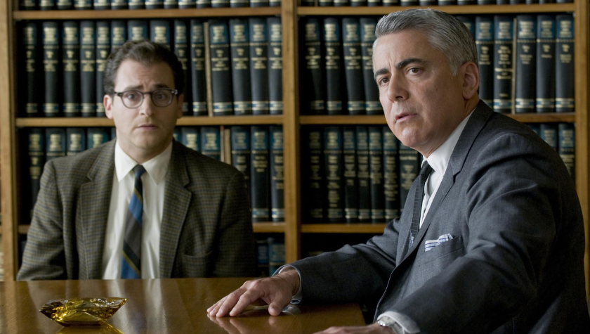 Adam Arkin and Michael Stuhlbarg wearing suits sit in an official office surrounded by books in 'A Serious Man'