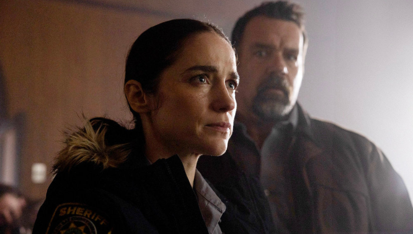 David James Elliott and Melanie Scrofano stand in a house surrounded by wooden walls in Revival