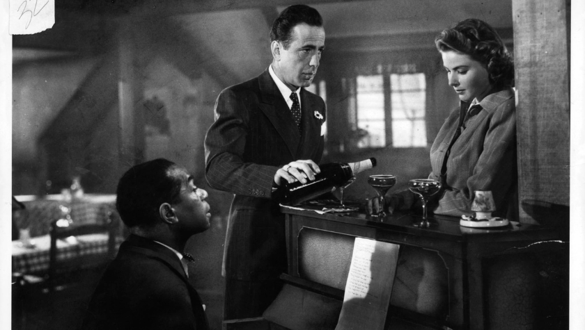 Humphrey Bogart pours Ingrid Bergman a glass of wine ontop of the piano as Dooley Wilson plays the keys in Casablanca