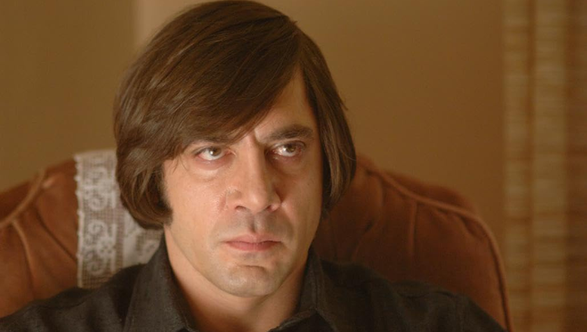 Javier Bardem sits in a red chair glaring