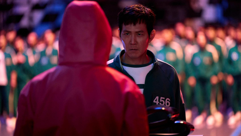 Lee Jung-jae stands in front of a crowd of contestants facing one of the regulators in Squid Game