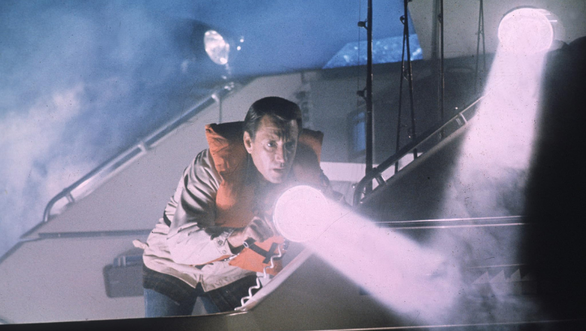 Roy Scheider wears his life jacket as he stands on a boat shining a light into the ocean in 'Jaws'