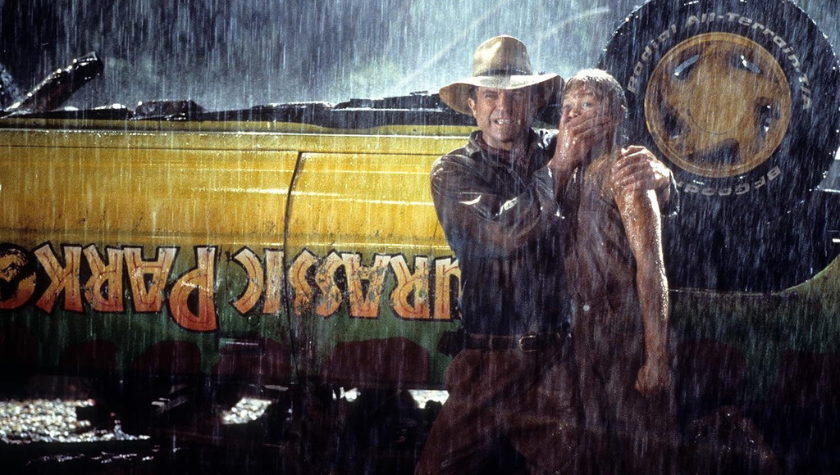 Sam Neill covers Ariana Richards' mouth while standing in the rain beside an upside-down Jeep in Jurassic Park