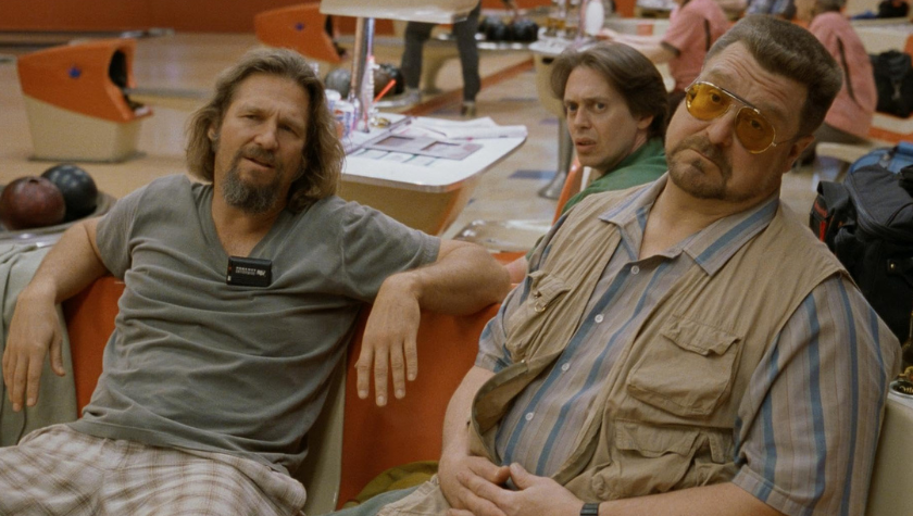 Steve Buscemi, Jeff Bridges, and John Goodman sitting at their bowling lane in a busy bowling alley in The Big Lebowski