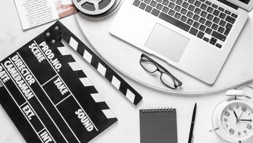 image of a desk with a clapper, laptop, film reel, glasses, and a white alarm clock