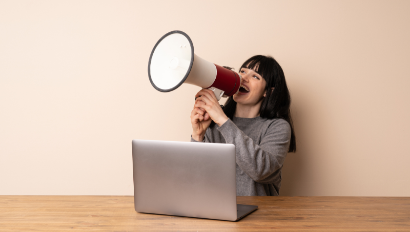 woman sitting at her laptop shouting with a megaphone